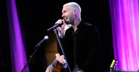 Adam Levine singing into a microphone on stage.