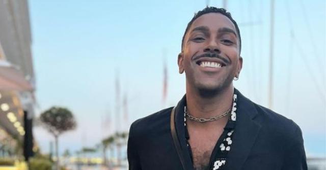 Johnathan Shillingford poses in a blue suit in front of the water