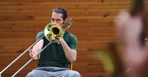A man in a green shirt blowing a trombone.