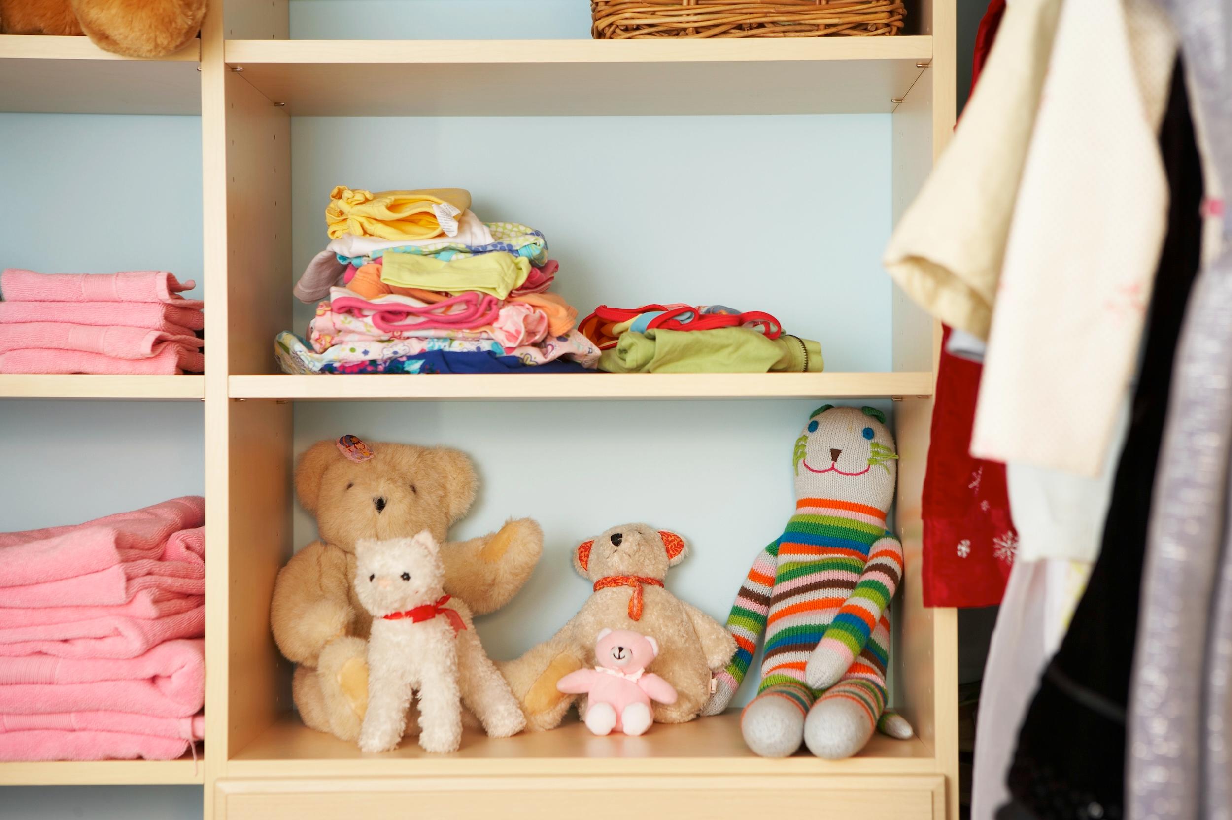 Stuffed animals, clothing, and towels on shelves in a nursery closet