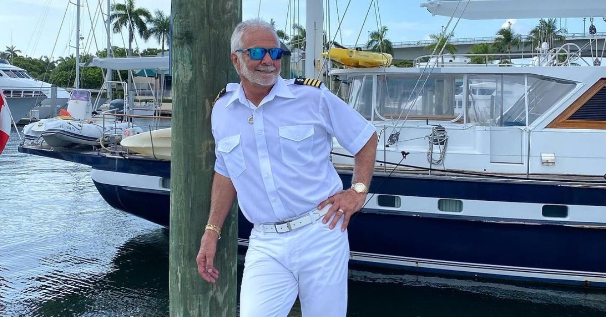 Below Deck's Captain lee leans up against a pole in front of boats on a dock