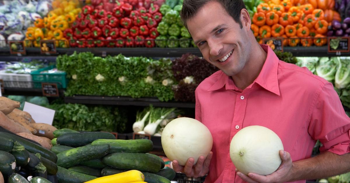 Man holding melons against chest, smiling, portrait, close-up - stock photo