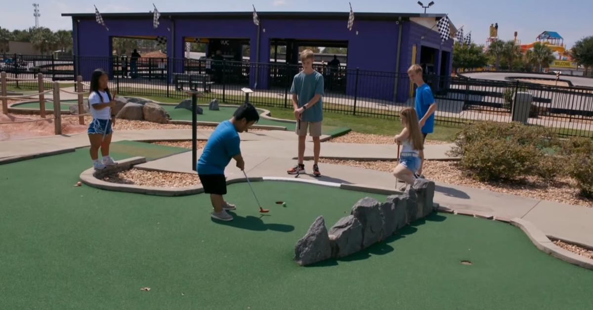 Alex hits the golf ball during a game of mini-golf with Emma and their friends Ella, Sean, and Ryan.