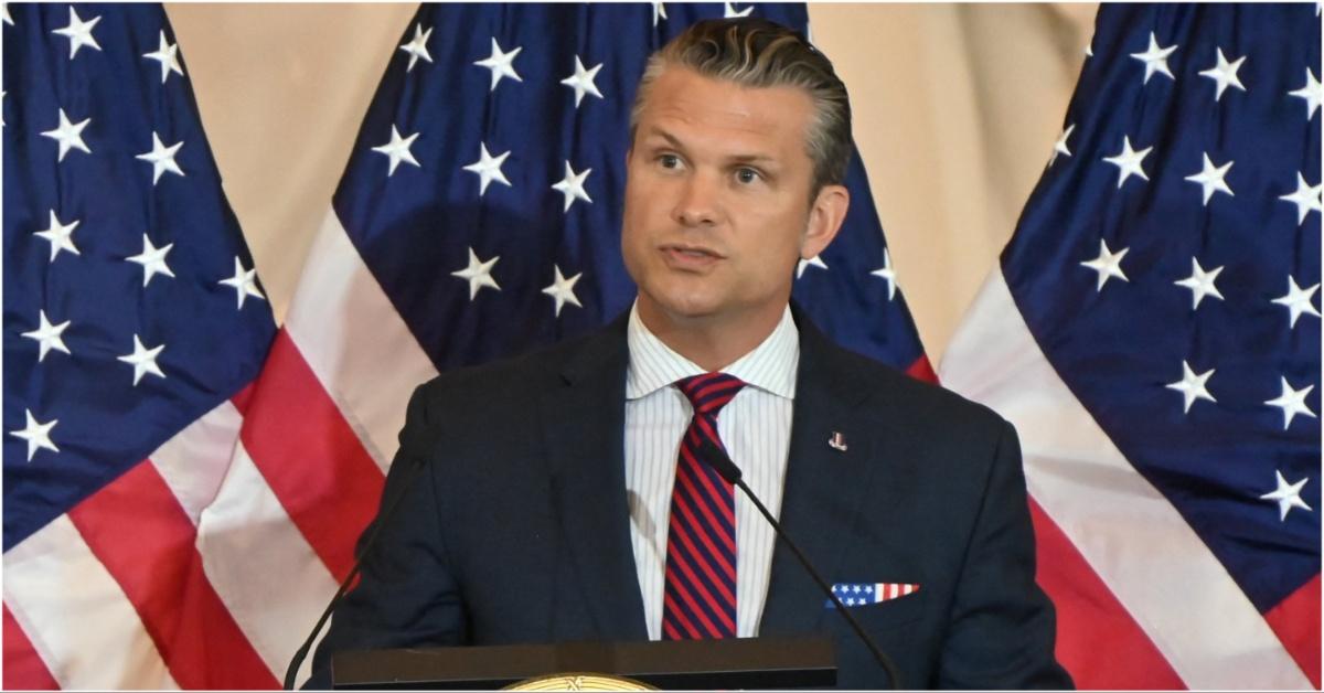 Pete Hegseth standing in front of American flags while speaking