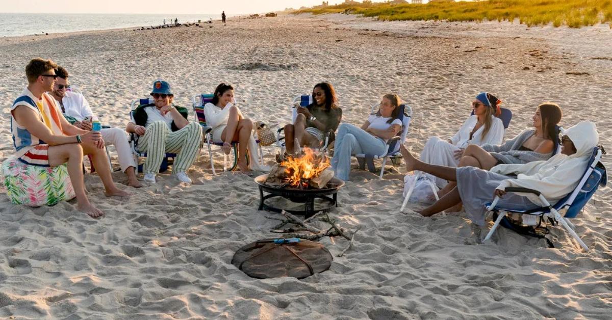 The Summer House cast sits on a beach with a fire.