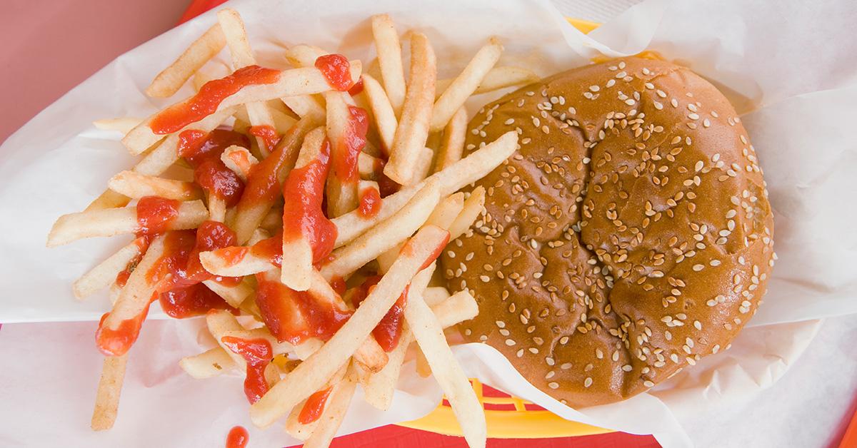 A burger sitting next to some fries with ketchup on them. 