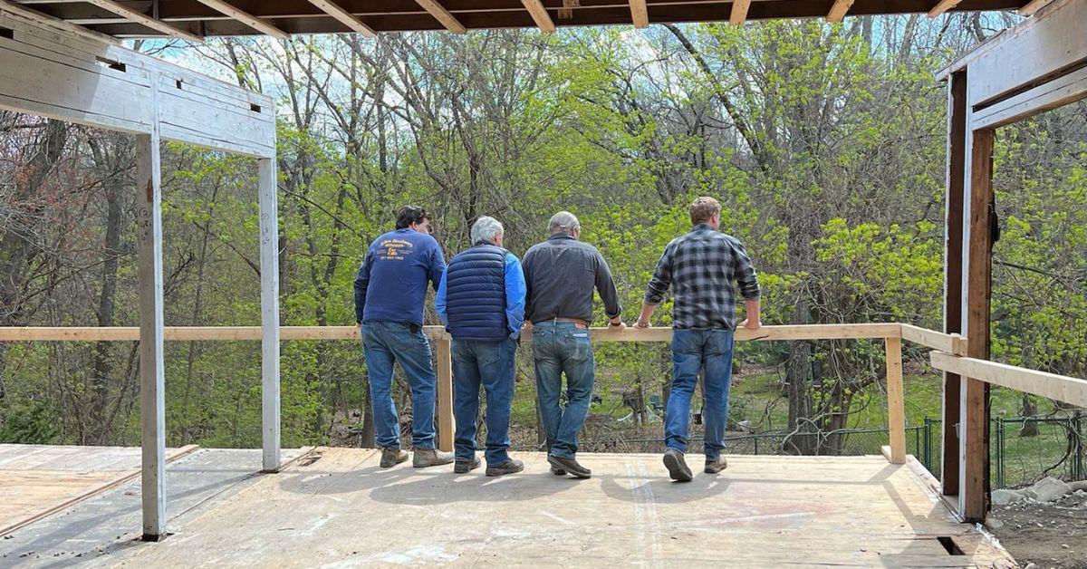 The 'This Old House' team overlooks a backyard while standing on a deck in progress