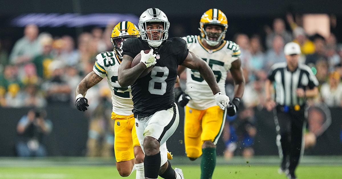 Josh Jacobs running with two Green Bay Packers behind him. 