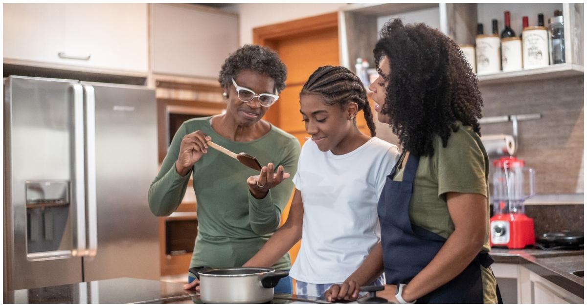 (l-r): An older woman, a young girl, and an adult woman cooking