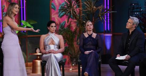 Lala Kent stands up speaking emphatically to Andy Cohen and Katie Maloney and Ariana Madix sit between them.
