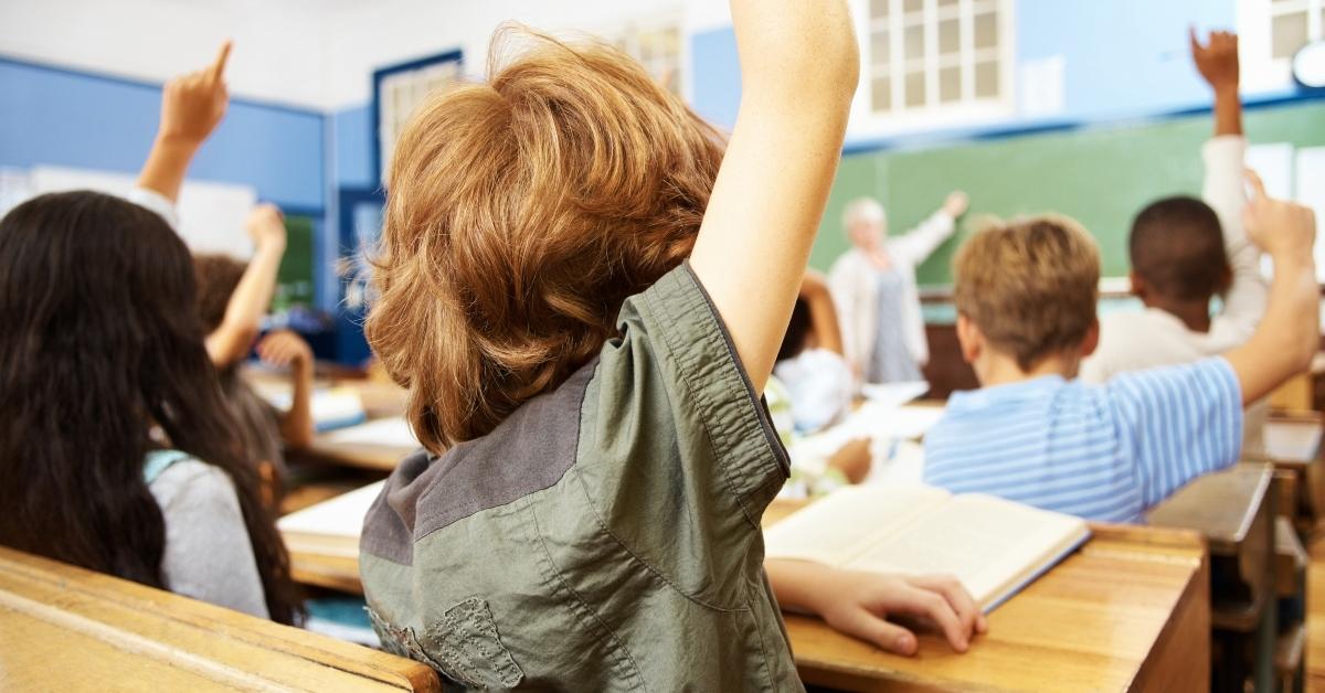 Elementary students raising hands in classroom - stock photo