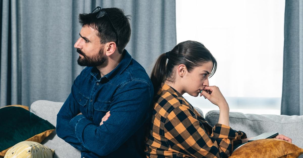 Young angry couple sit back to back on the couch in their home