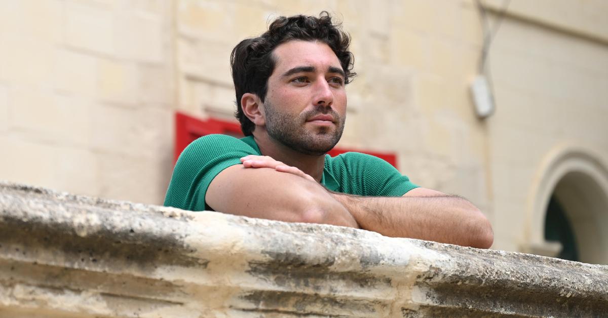 Joey Graziadei appears lost in thought while leaning over a railing in Season 28 of 'The Bachelor.'