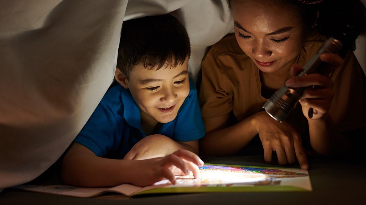 A woman and young boy using a flashlight or "torch" to read a book in the dark