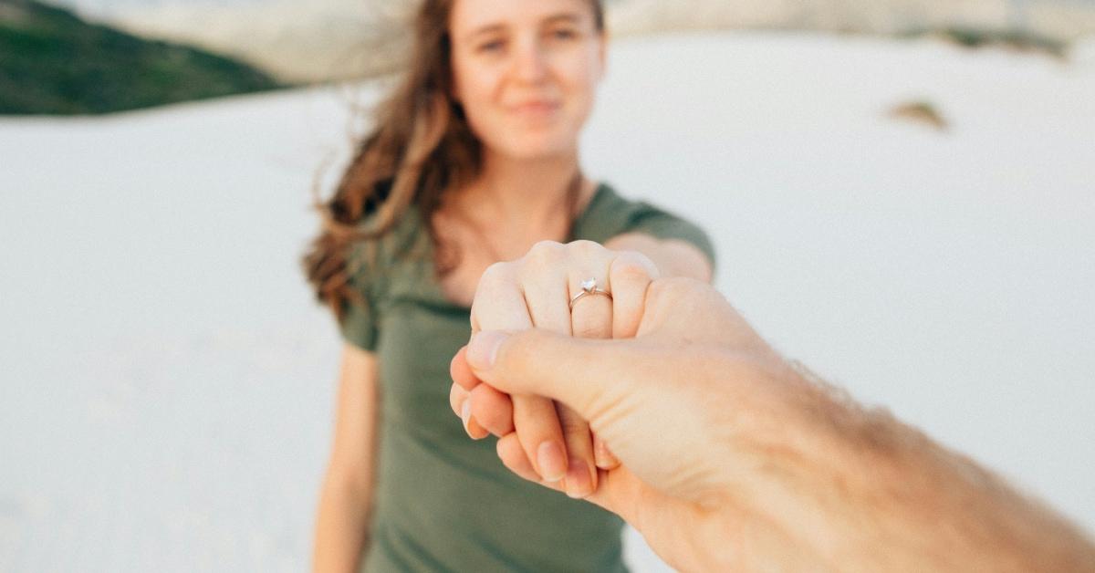 A guy holding his fiancé's hand with a gold ring on it.