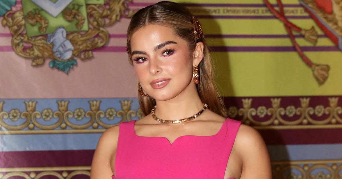 Addison Rae slightly smiles wearing a hot pink dress in front of patterned background.