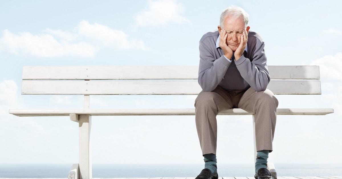 An unhappy old man sitting on a bench.