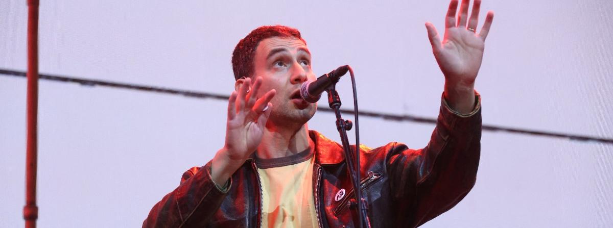 Jack Antonoff singing into a microphone and looking up into the stage lights