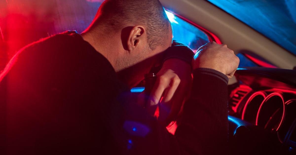 drunk man covering his face from police car light picture id