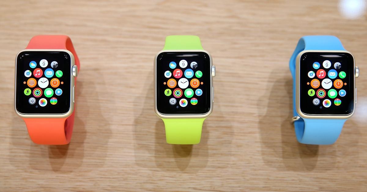 Orange, green, and blue Apple Watches on a wooden table.