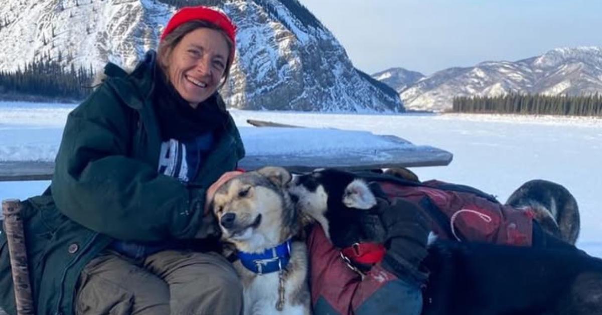 Denise Becker smiles in the snow as she pets two dogs.