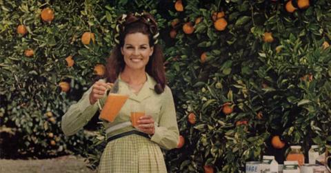 Abita Bryant holding orange juice with oranges behind her.
