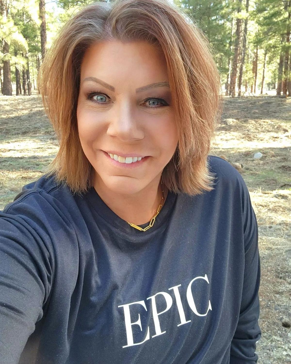 Meri Brown smiles outside wearing a black shirt that says "EPIC". 