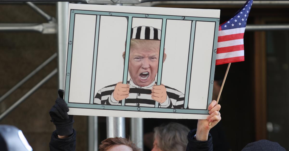 A protestor holds up a sign that depicts Donald Trump behind bars.