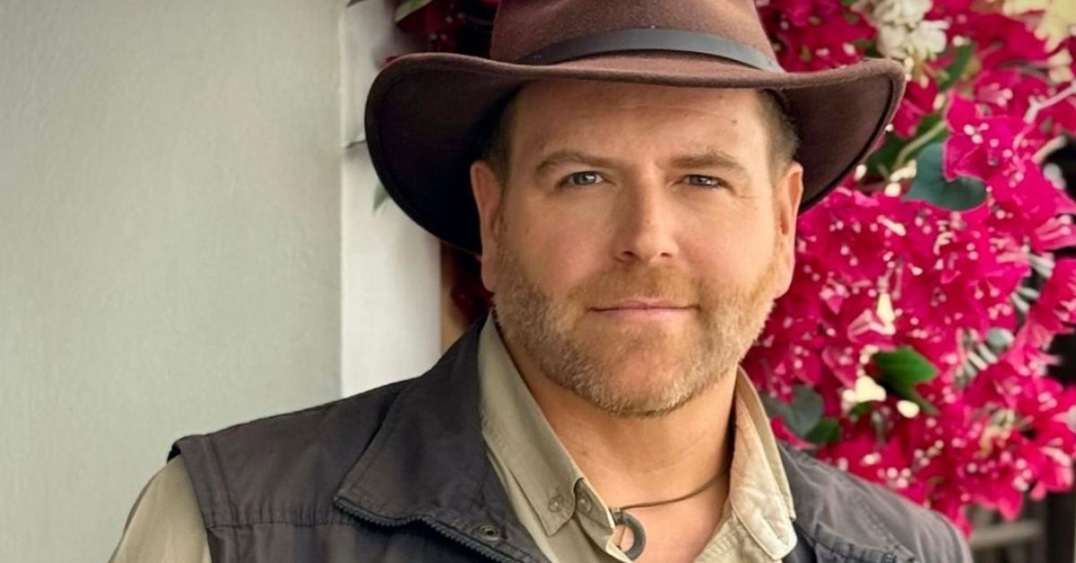 Josh Gates in his signature hat in front of flowers