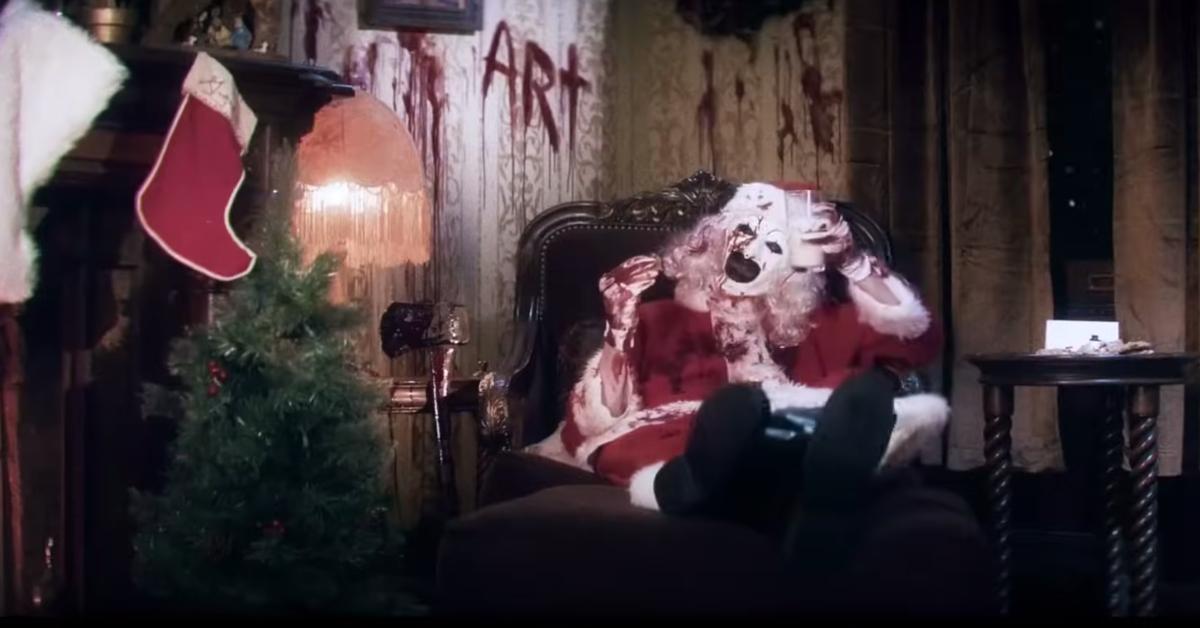 Art the Clown sitting in a chair and dressed as a bloody Santa Claus