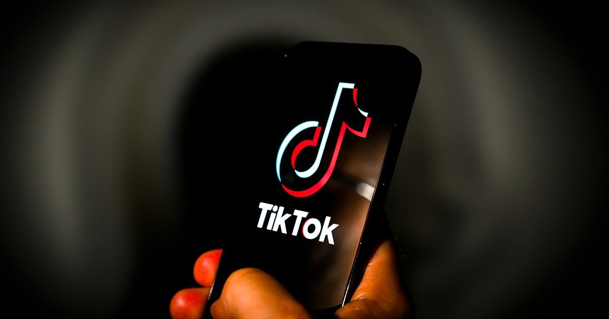 A person holding a phone with a TikTok logo on it. 