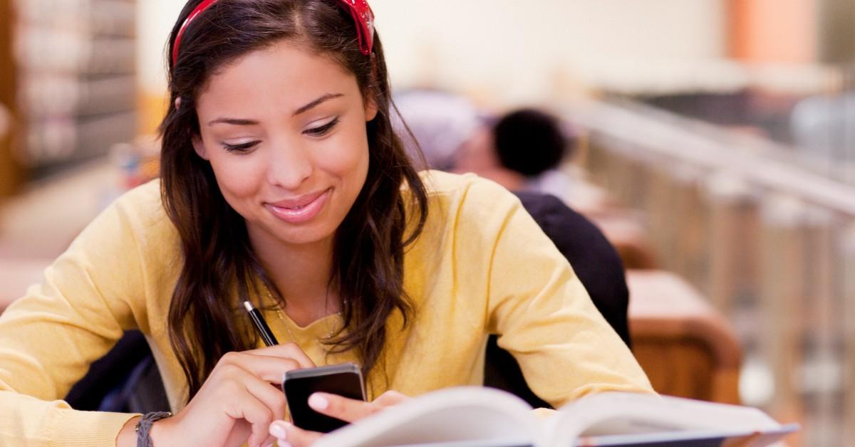 A student with long brown hair and a headband looks at a text. 