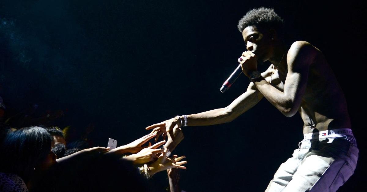 Rich Homie Quan performing and holding hands with someone in the crowd.