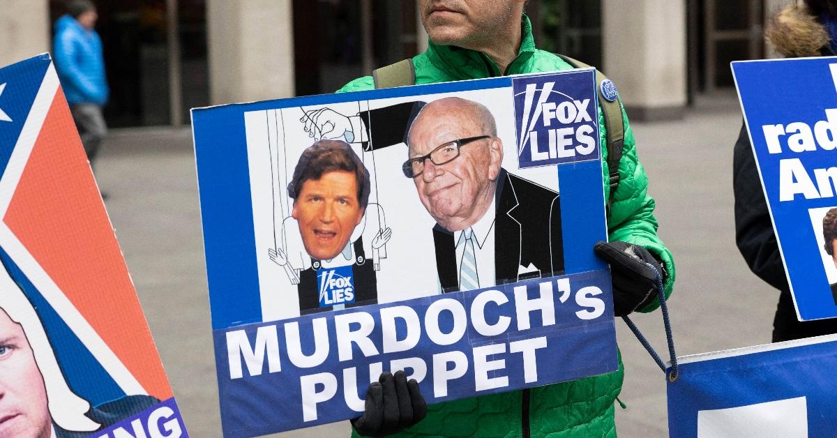 Protestor holds up a sign with Tucker Carlson and Rupert Murdoch on it