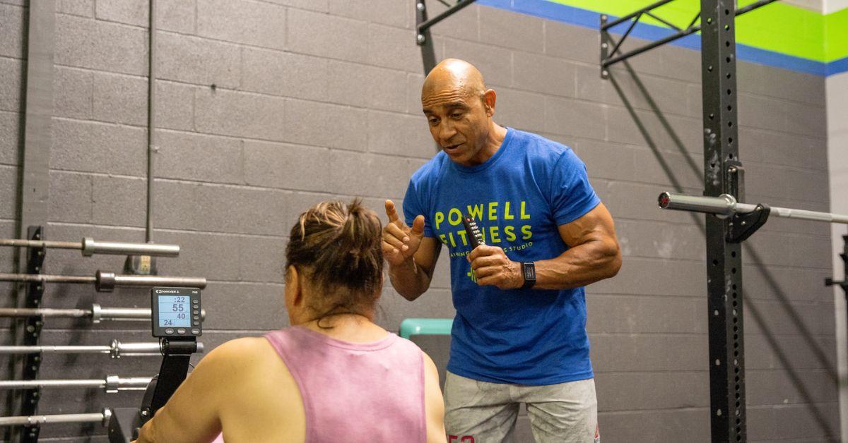William Powell coaching someone in a Powell Fitness t-shirt. 