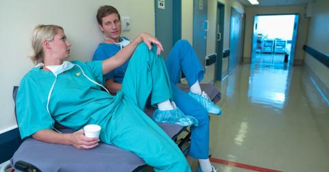 Two nurses sitting on a stretcher in a hospital hallway.