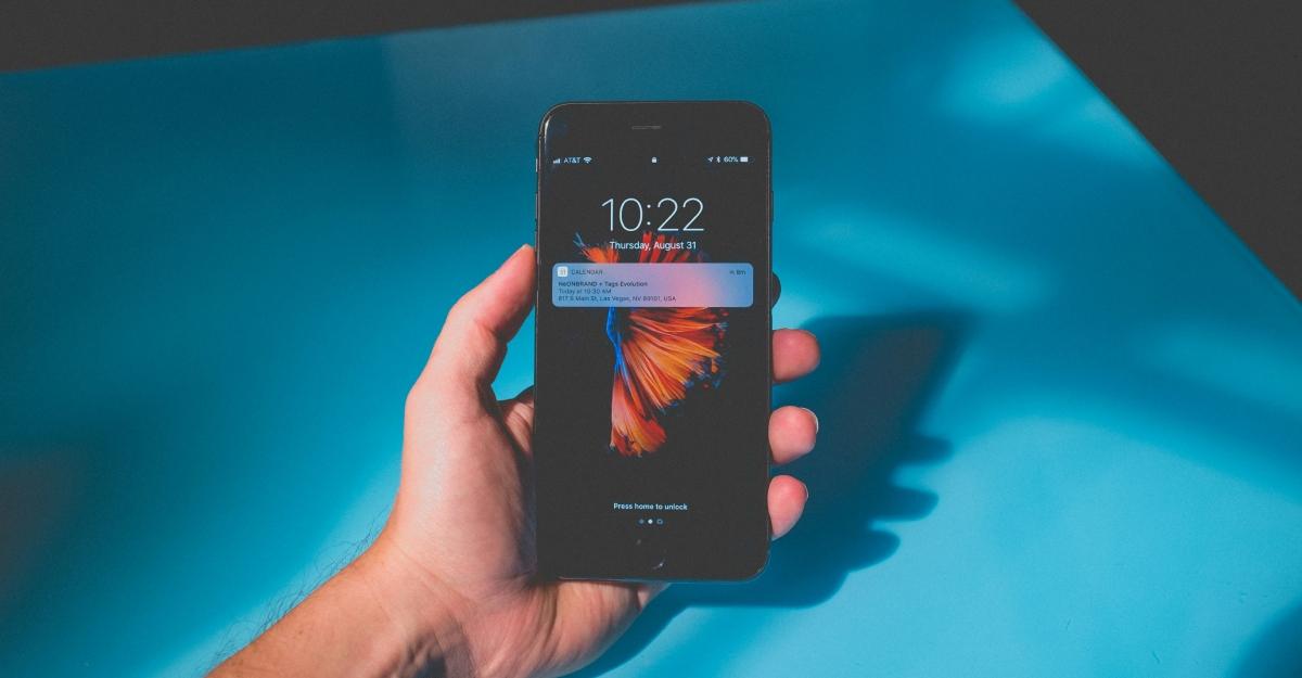 A hand holds an iPhone in front of a blue background. There is a notification on the lock screen.