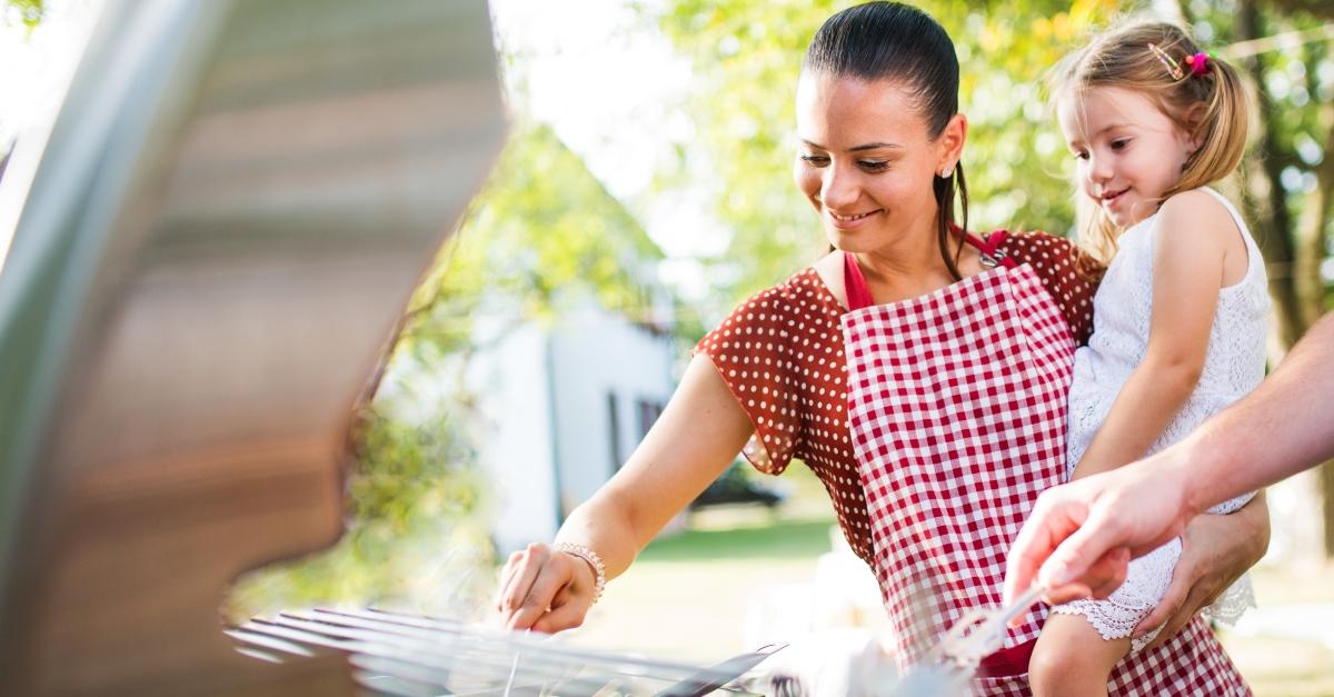 A woman holds her child in front of a grill