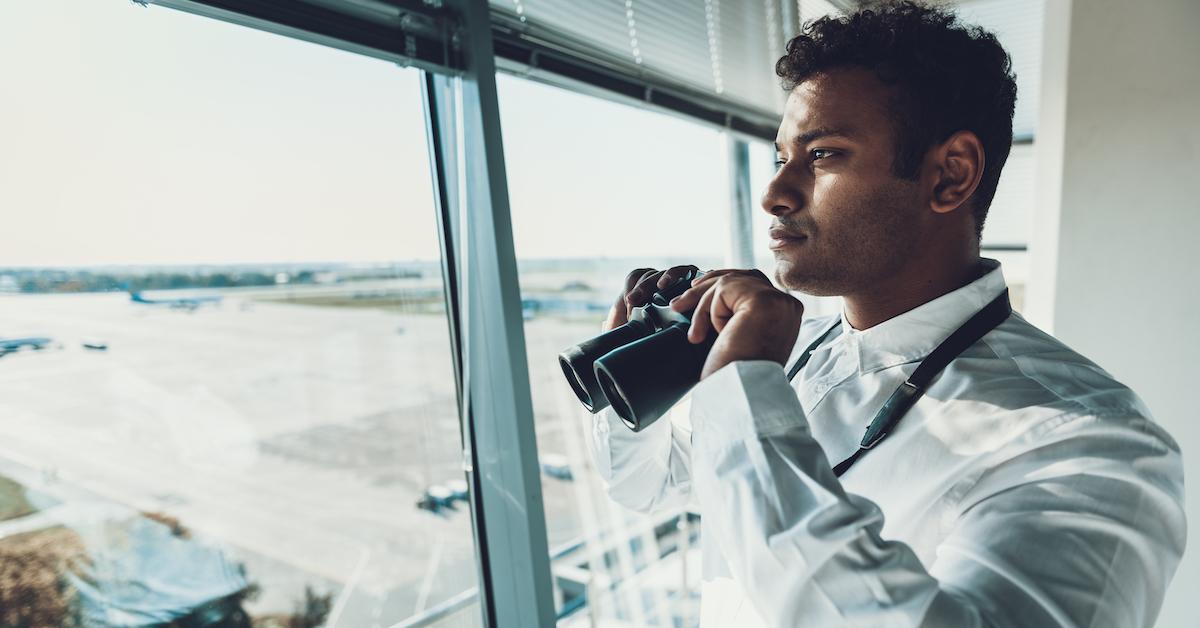 air traffic controller holds binoculars looking out at runway