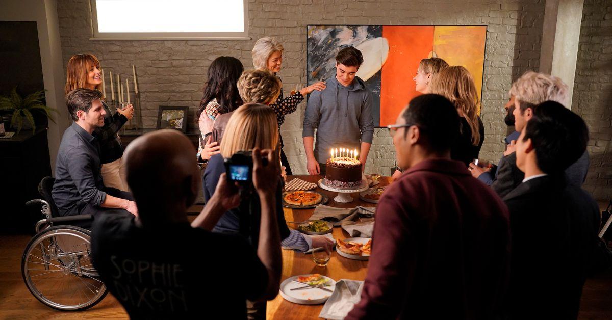 'A Million Little Things' characters celebrating a birthday party next to a chocolate cake.