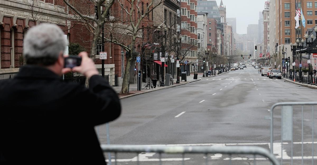 man stand behind barricades for Boston marathon taking a photo before the runners emerge